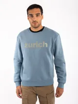 Sudadera celeste con cuello redondo, puños y cintura acanalados. Estampado frontal con la palabra "Zurich" en letras plateadas.