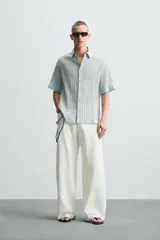 Camisa de manga corta con cuello solapa, confeccionada en tejido de mezcla de lyocell con textura de efecto arrugado y cierre frontal de botones.
