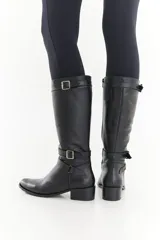 Bota de caña alta de cuero liso negro, con diseño clásico, detalles de hebillas metálicas, cierre lateral y taco bajo.