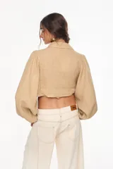 Top corto de lino italiano con diseño a cuadros en tonos verde oliva, beige y rosado, cuello camisero, mangas largas abullonadas con puños elásticos y nudo frontal ajustable.