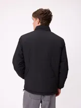 Campera reversible de nylon con cuello alto y cierre frontal. Un lado es de color gris liso con logo bordado, mientras que el otro lado presenta un estampado abstracto en tonos azules. Cuenta con bolsillos laterales y puños elásticos.