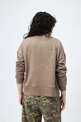 Buzo color marrón de corte relajado confeccionado en tejido de algodón con interior suave al tacto. Presenta detalle de estrella con tachas en la espalda y bordado delantero con la frase Dreamer – Born to rock.