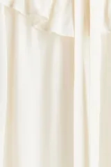 Blusa de crepé color blanco roto, con cuello alto de volado y tiras para atar en el frente. Tiene mangas largas abullonadas con puños abotonados y ribete de volado. El canesú es de doble capa con diseño en V y ribete de volado.