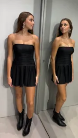 Vestido corto negro strapless, con diseño ajustado fruncido en el torso y falda corta con vuelo.