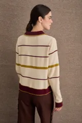 Buzo de punto con cuello polo y cierre frontal de tres botones. Diseño a rayas horizontales en tonos crema, bordó y mostaza, con detalle de bordado en el pecho.