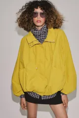 Cazadora bomber de cuello subido ajustable con cordones, manga larga con puños elásticos y cierre frontal con cremallera y botones a presión ocultos bajo solapa. Cuenta con bolsillos delanteros y diseño holgado.