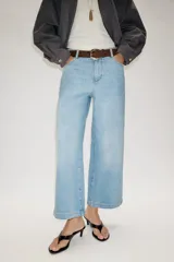Jeans de tiro alto con pernera ancha y corte cropped. Presenta diseño de cinco bolsillos, cierre frontal con cremallera y botón, e incluye un cinturón de gamuza marrón con hebilla metálica.