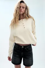 Bermuda de tiro medio confeccionada en denim de color negro gastado, con diseño de cinco bolsillos, trabillas para cinturón y cierre frontal con cremallera y botón metálico.