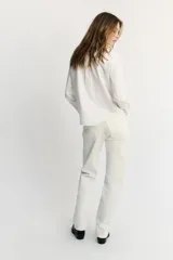 Camisa blanca de manga larga con cuello redondo tipo bebé y cierre frontal de botonadura simple.