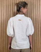 Camisa de algodón a rayas color beige y blanco, con escote en V, cuello mao y mangas cortas abullonadas. Cuenta con cierre frontal de botones oscuros.