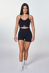 Conjunto deportivo de dos piezas en color negro, compuesto por un top con espalda descubierta y tiras cruzadas, y un short de tiro alto con efecto fruncido en la parte posterior. El short presenta el logo de la marca estampado en la cintura.