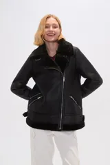 Campera de estilo aviador confeccionada en eco-cuero negro con interior de piel sintética oscura. Presenta cierre frontal cruzado, solapas amplias, bolsillos laterales con cierre y detalles de hebillas ajustables en los puños.