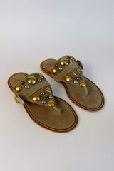 Sandalia plana de gamuza marrón, estilo ojota, con apliques metálicos dorados y hebilla decorativa.