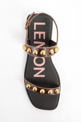 Sandalias planas de cuero marrón con tiras decoradas con tachas semiesféricas doradas, talón cerrado con tira ajustable y hebilla metálica.