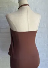Vestido corto marrón oscuro, estilo halter con cuello anudado en una argolla central. Presenta un diseño drapeado en la parte superior que cae sobre una falda ajustada.