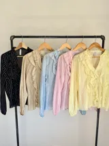 Camisa de organdí rosa pastel con finas rayas verticales metalizadas, escote en V con volados frontales y mangas largas abullonadas con puños elásticos.