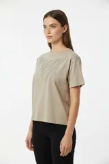 Remera de algodón color beige, manga corta y cuello redondo a la base. Presenta un diseño abstracto de líneas curvas formado por pequeños apliques brillantes (studs) en la parte superior delantera.