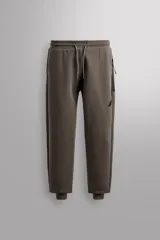 Pantalón jogger de entrenamiento, corte regular fit, color verde oliva oscuro. Confeccionado en tejido técnico compacto de algodón con elasticidad y efecto neopreno. Presenta cintura elástica ajustable con cordón blanco, bolsillos frontales y un bolsillo lateral con cierre de cremallera. El bajo termina en puño.