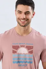 Remera de manga corta color rosado, con cuello redondo y estampa frontal de diseño playero y la inscripción "Travel. Beach. Repeat. LEGACY".