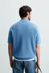 Polo de manga corta, color azul medio, tejido en punto perlado con cuello solapa y cierre frontal de cremallera.