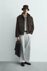 Cazadora de corte relajado confeccionada en piel con acabado de ante. Presenta cuello subido, cierre frontal de cremallera oculta por solapa con botones a presión, bolsillos de plastrón con solapa en el pecho y bolsillos de vivo en la cadera. Incluye trabillas en los hombros, mangas largas con puños abotonados y bajo con elástico.