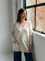 Sweater de punto color beige, con cuello en V, mangas largas con puños acanalados y dos bolsillos frontales. Presenta una costura vertical central y un diseño holgado.