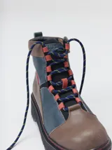 Bota de estilo trekking con diseño multicolor en tonos marrón, azul y detalles en rojo. Presenta plataforma de goma dentada, cordones tipo cuerda de escalada y cuello acolchado.