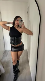 Corset de un solo hombro con cuerpo superior de tela lisa y sección inferior de cuero sintético con cordones frontales ajustables mediante ojales metálicos.