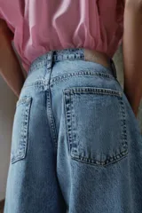 Pantalón de jean tiro medio con diseño barrel, caracterizado por su pernera holgada que se estrecha hacia el tobillo. Presenta cinco bolsillos, cierre frontal con cremallera y botón, y detalle de raya planchada en el frente.