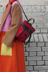 Mochila pequeña color borgoña con detalles en cuero marrón y aplique metálico de un caballo. Tiene manija superior y correas traseras regulables.