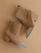 Bota texana de gamuza color beige, con puntera en punta decorada con strass plateado. Presenta un diseño de caña media con elásticos laterales y taco cuadrado de estilo western.