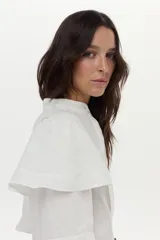 Camisa blanca de lino con cuello mao, volados en los hombros y mangas abullonadas con elástico. Cierre frontal con botones.