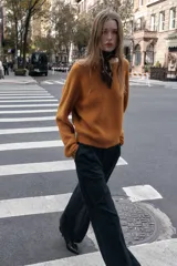 Jersey de punto color naranja quemado, de manga larga y cuello redondo. Presenta un detalle de nudo en la espalda.