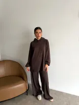 Conjunto de dos piezas compuesto por un buzo con capucha de corte holgado y mangas largas, y un pantalón de corte recto y tiro alto. Ambas prendas son de color marrón liso.