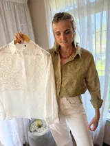 Camisa de manga larga color verde militar, con cuello clásico y cierre frontal de botones. Presenta un canesú bordado con diseño ornamental en la parte frontal superior.