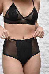 Bombacha de tiro alto confeccionada en microtul negro, con panel central frontal de encaje floral y detalles de ondas en los bordes.