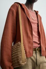 Bandolera color beige con acabado trenzado, compartimento principal con cierre de cremallera, bolsillo plano interior y asa de hombro ajustable.