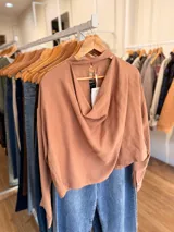 Blusa de color terracota con escote drapeado y detalle de cinta al cuello. Presenta un diseño holgado de manga larga con puños abotonados.