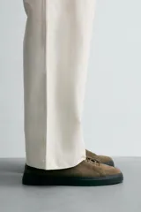 Zapatilla de estilo urbano confeccionada en piel con acabado de serraje. Presenta un diseño minimalista con cordonera oculta y suela de goma a contraste.