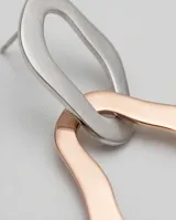 Caravanas colgantes de diseño geométrico irregular, compuestas por dos eslabones entrelazados, uno en tono blanco y otro en baño de oro rosa.