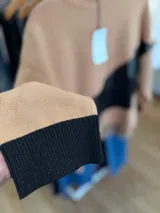 Buzo de tejido de punto con diseño oversize y calce relajado. Presenta un diseño de bloques de color en tonos neutros con una franja diagonal central en material metalizado brillante. Cuenta con cuello redondo y mangas largas con puños acanalados.