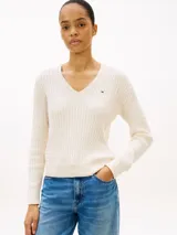 Sweater de punto trenzado color blanco de Tommy Hilfiger, con cuello en V, mangas largas y detalles acanalados en puños y dobladillo. Presenta el logo de la marca bordado en el pecho.