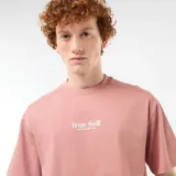 Remera rosada de corte oversize con cuello redondo, manga corta y pequeño bordado frontal con el texto "True Self".