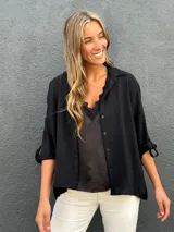 Camisa oversize color negro, con cuello camisero, cierre frontal con botones y mangas largas con presillas para arremangar.