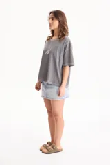 Remera de algodón gris con efecto lavado, corte semi boxy, mangas cortas y costuras en contraste. Presenta un pequeño bordado frontal con líneas curvas y la palabra "Ciao".