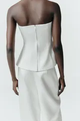 Top strapless de satén color blanco, con diseño entallado y detalle de dos lazos decorativos en el frente. Presenta aberturas en el bajo y cierre posterior con cremallera.