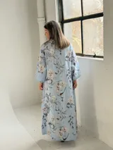 Vestido largo celeste con estampado floral en tonos blancos y grises, de corte holgado, mangas largas y cuello drapeado.