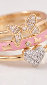 Set de tres anillos apilables de plata 925 con baño de oro. Incluye un anillo con dije de corazón pavé de circonias, un anillo con esmalte rosa y detalles de corazones, y un anillo con diseño de lazo de Minnie Mouse decorado con circonias.