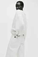 Pantalón jean de denim de algodón rígido, color blanco, de corte wide leg con tiro alto, bolsillos delanteros con ribete trenzado y pliegues marcados.