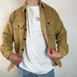 Sobrecamisa de pana en color tostado, con cierre frontal de botones, cuello clásico y dos bolsillos frontales con solapa y botón.